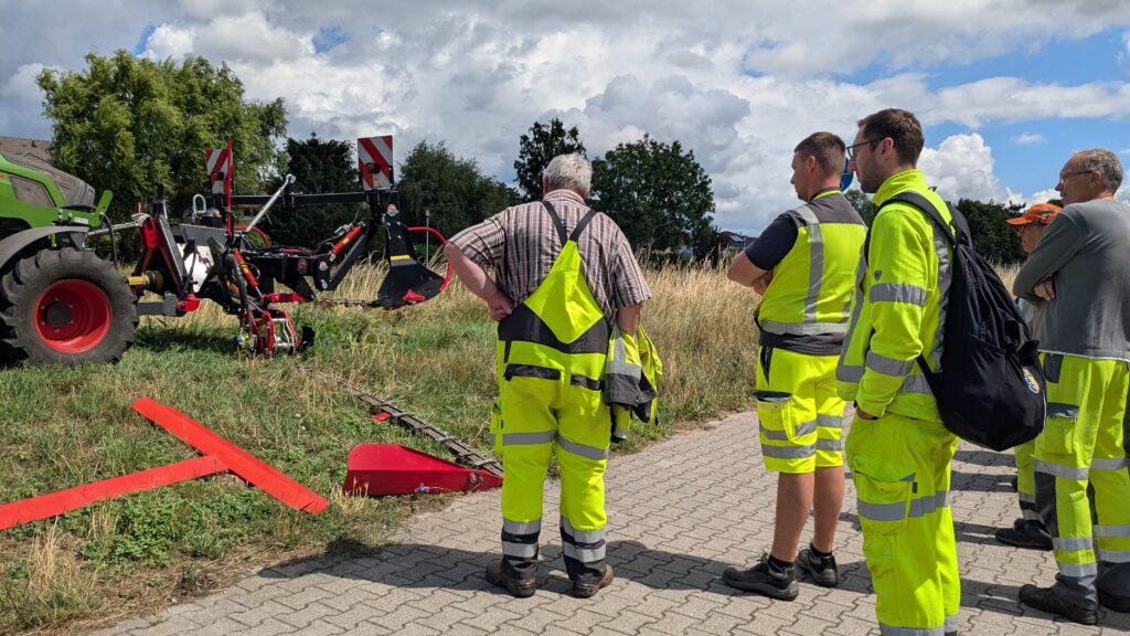 Personen schauen sich Mähwerk an einem Traktor an