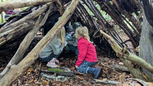 Kinder knien in einem Shelter aus Baumstämmen im Wald