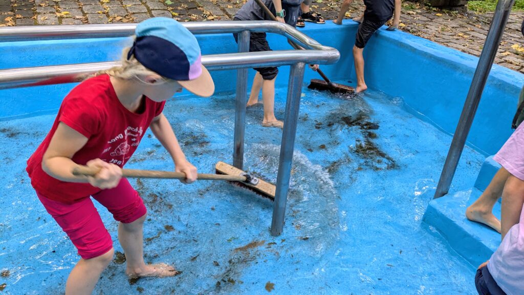 Kind schrubbt mit Besen Boden in Kneippbecken