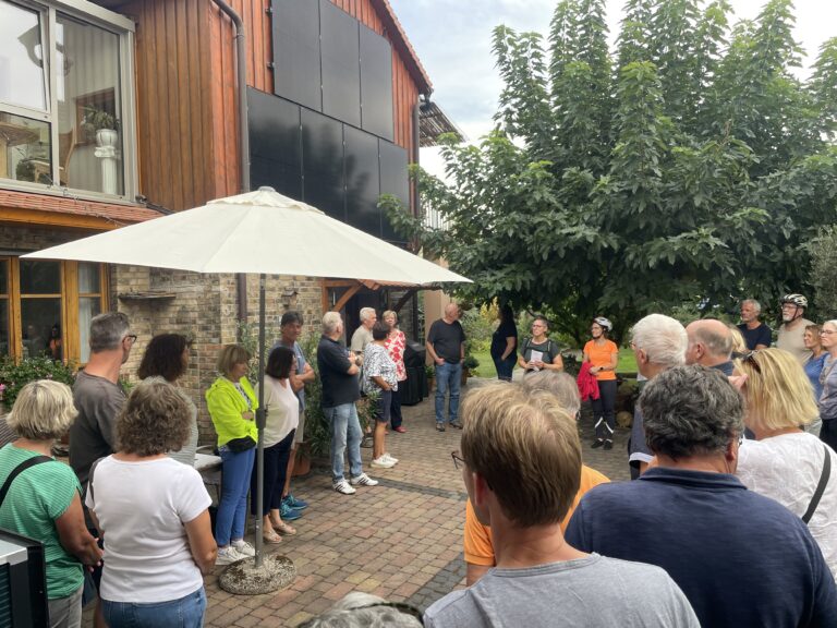 Menschen stehen in einem Garten und hören Erklärungen zu.